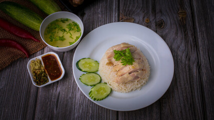 Hainanese chicken rice or Khao Man Gai Asian food in a wood white plate with delicious broth and dipping sauce.