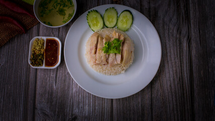 Hainanese chicken rice or Khao Man Gai Asian food in a wood white plate with delicious broth and dipping sauce.