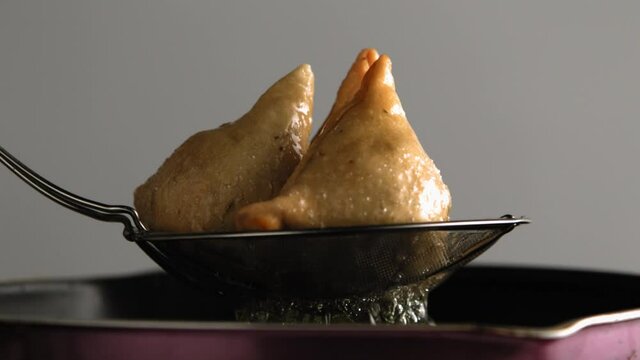 Boiling hot Samosas coming out of oil in frying utensil. Delicious Indian fried patties fresh out of the frying pan. Indian delicacy (fried pastry) in ultra slow motion . Stylised food shot. 