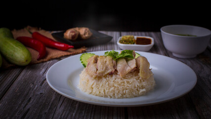 Hainanese chicken rice or Khao Man Gai Asian food in a wood white plate with delicious broth and dipping sauce.