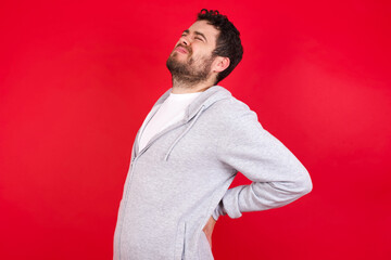young handsome caucasian man in sports clothes against red background got back pain