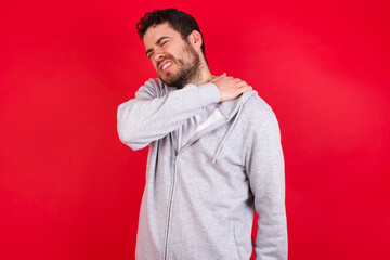 young handsome caucasian man in sports clothes against red background got back pain