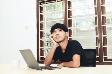 Obraz premium An Asian man is sitting in front of the laptop with a thoughtful expression