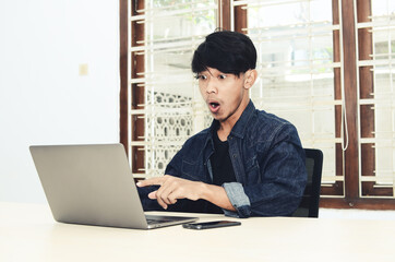 Fototapeta premium The Asian man sat in front of the laptop with a shocked expression
