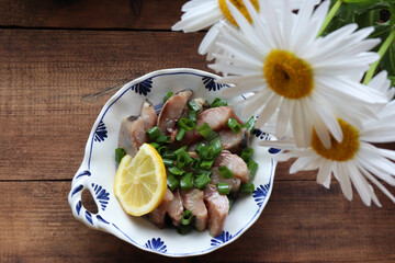 Pieces of salted herring fish on a plate with green onion and lemon slice. Swedish pickled herring on wooden table background. Midsummer traditional food. Top view, copy space	