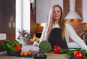 A young happy lady standing in the kitchen while cooking.
