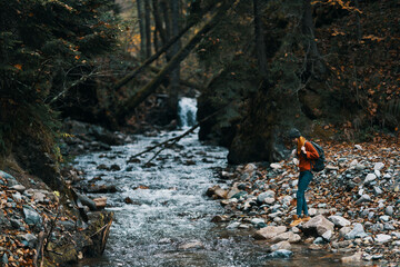 woman tourist with a backpack walked along the bank near the river, a stream of water and tall trees