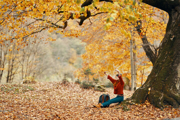 woman with a backpack under a tree in the park and falling leaves autumn landscape