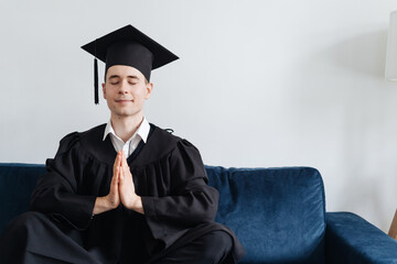 Education, graduation and people concept - happy male student sitting in yoga pose on blue couch at home showing his emotions. Meditation