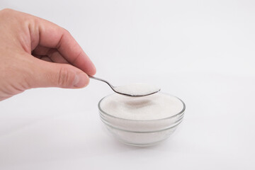 female hand holds a spoon with sugar. Sugar - sand in a glass bowl and spoon on a white background.