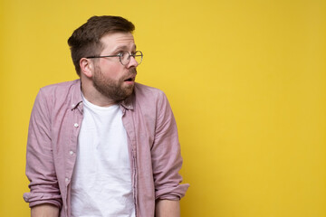 Frightened Caucasian man wearing glasses and casual clothes looks anxiously to the side. Copy space. Yellow background.