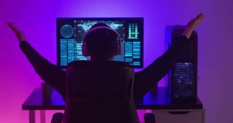 Man programmer in headphones happy with success while working at a computer in data center at night. Dangerous hacker working in cyber security center filled with neon light. - Powered by Adobe