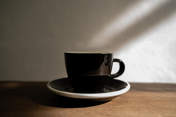 Black cup on a wooden table, Beautiful light and shadow on the white wall, Black Ceramic mug, coffee break in morning, selective focus, latte, Horizontal orientation, copy space