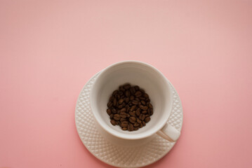White cup and saucer with black coffee beans on a bright pink background