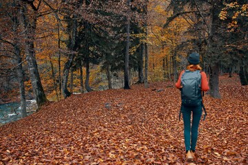 woman tourist with a backpack walking in the park with fallen leaves in autumn in nature