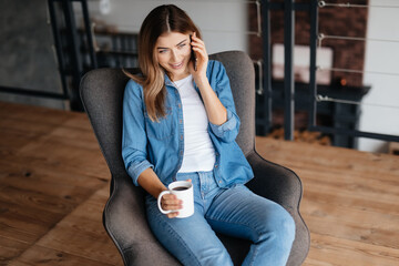 Smiley young woman talking on phone and drinking coffee
