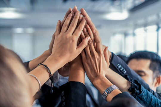 Many happy business people raise hands together with joy and success. Company employee celebrate after finishing successful work project. Corporate partnership and achievement concept.