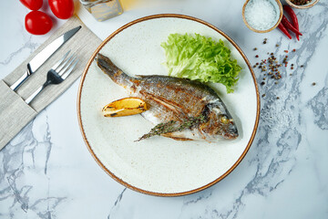 Appetizing and dietary grilled dorado, served in a white plate on a marble background. Top view