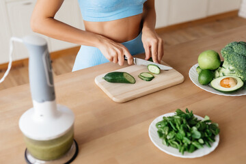 Obraz na płótnie Canvas Healthy lady cutting cucumber on wooden board at home