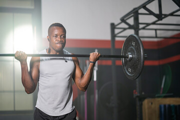 Fototapeta premium Strong adult black African men lift barbell to do crossfit exercise and weight lifting inside of fitness gym to workout for body strength and firm arms muscle and good physical body health.