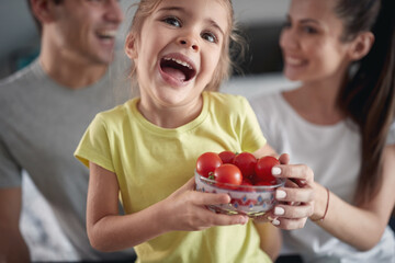 A little girl with her parents posing for a photo with a bowl full of cherry tomatoes at home....