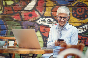 An elderly woman using a smartphone while spending free time at bar's garden. Leisure, bar, friendship, outdoor