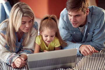 Mom and Dad teaching their little daughter at home how to use a computer. Family, home, togethernes