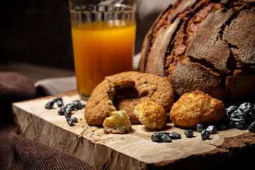 Biscuits, bread and a glass of juice on a wooden stand on a brown background