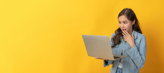 young asian pretty woman exciting with laptop computer on copy space area on yellow panoramic wide background, business finance, online marketing, entertainment and internet technology concept