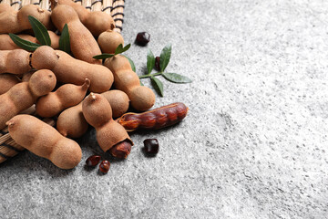Delicious ripe tamarinds and leaves on grey table. Space for text