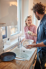 young caucasian couple having fun while washing dishes