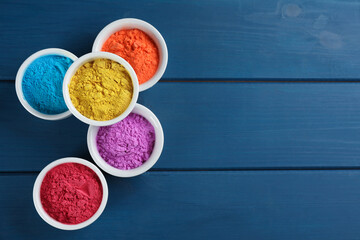 Colorful powder dyes on blue wooden background, flat lay with space for text. Holi festival