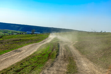 Fototapeta na wymiar Car on country road raises dust . Rural journey 