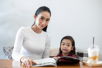 Asian mothers are teaching their daughters to read a book on holidays at home. Educational concepts and activities of the family