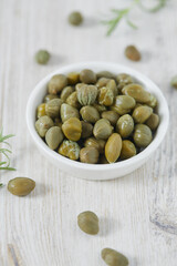 Pickled capers on white wooden surface. Gourmet food.