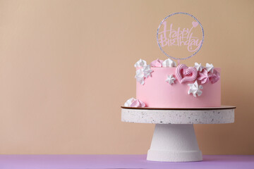 Beautifully decorated birthday cake on violet table near beige wall, space for text