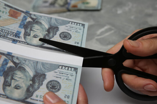 Counterfeiter cutting dollar banknotes with scissors at grey marble table, closeup. Fake money