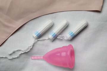 Woman's panties, tampons and menstrual cup on white fabric, flat lay