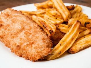 Traditional fish and chips dish on white plate. Common take away meal in English speaking nations. Cooked cod with peppered potato fries. Close up