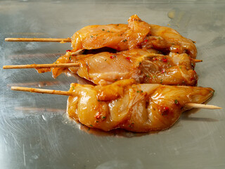 Marinated raw chicken pieces on a wooden skewer on a metal surface. Summer barbeque range product. Asian style sous over poultry meat.