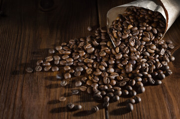 Roasted coffee beans lie in a paper bag and are scattered on a wooden background. View from above