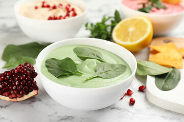 Bowl of delicious green hummus with spinach on white marble table