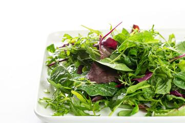 salad mix of fresh herbs, arugula, chard, spinach in a plate on a white plate, top-side view