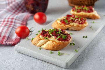 Sandwich with homemade mayonnaise, sun-dried tomatoes and micro greens, served on a board on a gray background