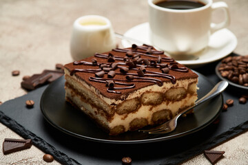 Portion of Traditional Italian Tiramisu dessert and cup of espresso coffee on grey concrete background