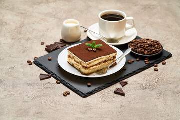 Portion of Traditional Italian Tiramisu dessert and cup of espresso coffee on grey concrete background
