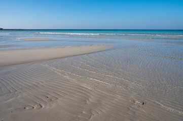 Sabbia bianca con mare trasparente e cielo azzurro.
