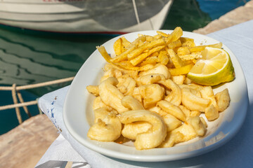 Grilled fresh squid on white plate with lemon and chips.