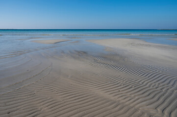 Sabbia bianca con mare trasparente e cielo azzurro.