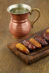 Ramadan iftar food, delicious date fruits on wooden plate and drinking water in a copper mug. 
